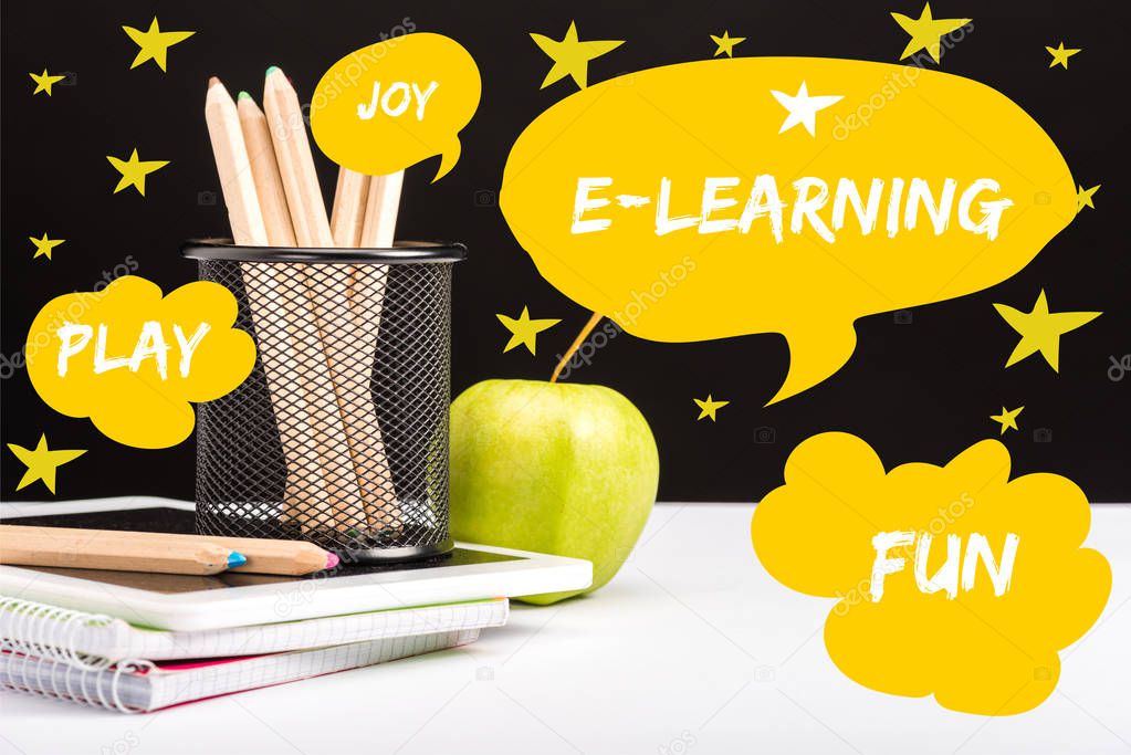 fresh apple, notebooks and color pencils on table with e-learning and joy words  in yellow speech bubbles and play and fun words in clouds with stars around on black 