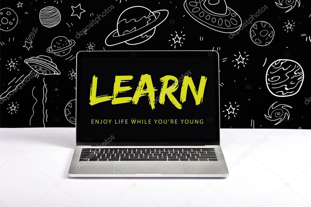 laptop on table with enjoy life while you are young and learn lettering on screen with white space illustration on black 