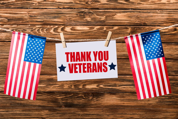 card with thank you veterans lettering hanging on string with pins and american flags on wooden background