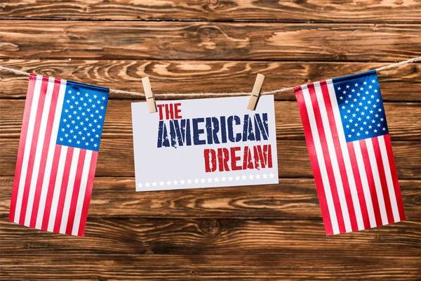 card with the american dream lettering hanging on string with pins and american flags on wooden background