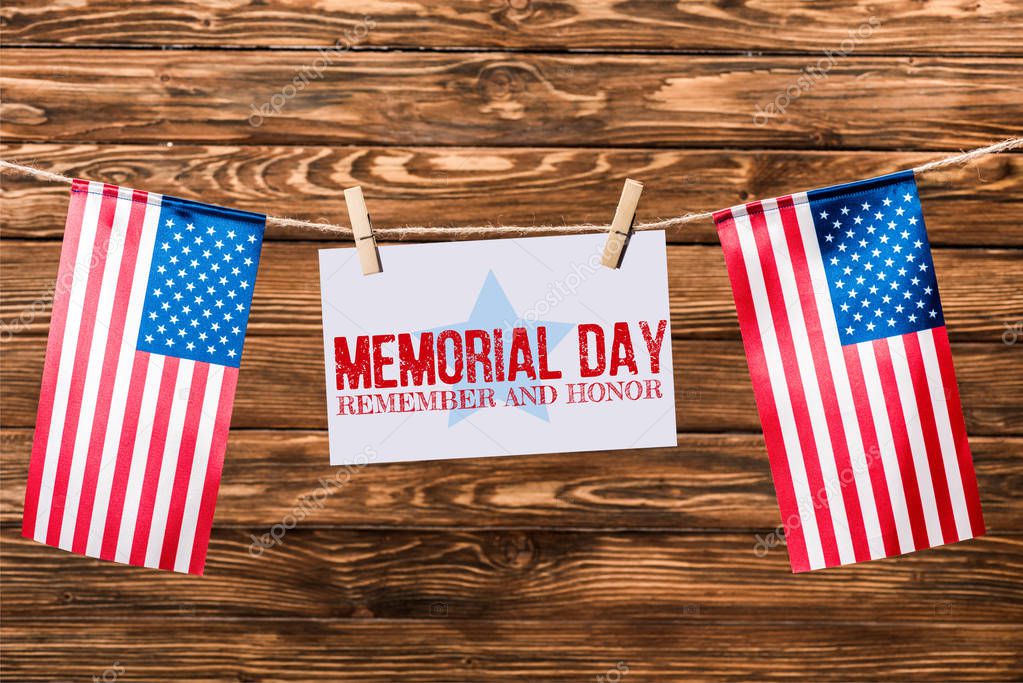 card with memorial day lettering hanging on string with pins and american flags on wooden background