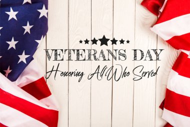 top view of american flags and veterans day lettering on white wooden surface clipart