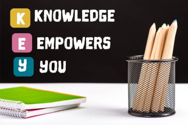 notebooks and color pencils on table with key and knowledge empowers you lettering on black   clipart