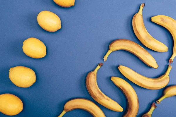 파란색 배경에 노란색 레몬과 신선한 바나나의 상단보기 — 스톡 사진