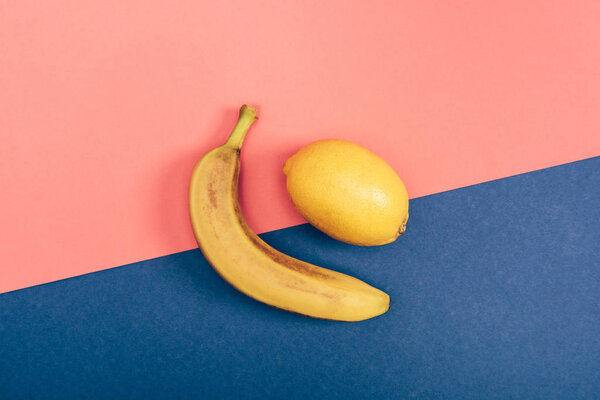 Top view of yellow banana and juicy lemon on multicolored coral and blue background