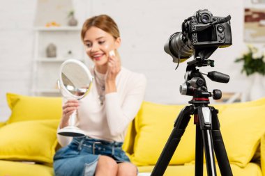video kamera önünde dekoratif kozmetik kullanarak ayna ile gülümseyen güzellik blogger seçici odak