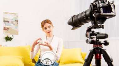 blogger sarı kanepede oturan ve video kamera önünde parfüm tutan