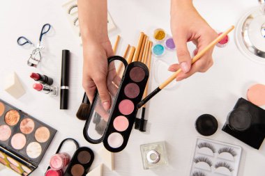 cropped view of woman holding eyeshadows and cosmetic brush clipart