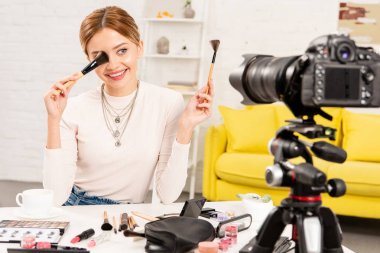 gülümseyen güzellik blogger video kamera önünde kozmetik fırçalar tutarak