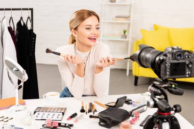 gülümseyen güzellik blogger video kamera önünde kozmetik fırçalar tutarak