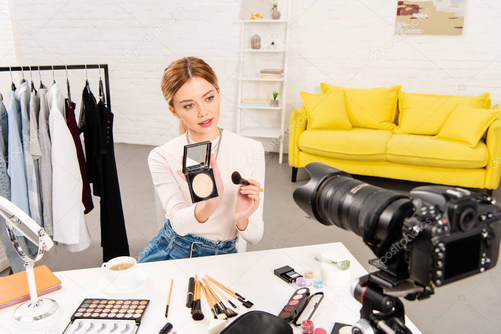 beauty blogger showing face powder and cosmetic brush in front of video camera