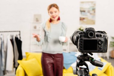 selective focus of blogger holding cup of coffee in front of video camera clipart