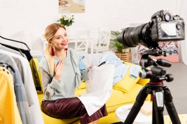 gülümseyen blogger kanepede oturan ve video kamera önünde giysi gösteren