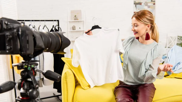Uśmiechnięty Blogger Siedzi Żółtej Kanapie Pokazując Ubrania Przed Kamerą Wideo — Zdjęcie stockowe