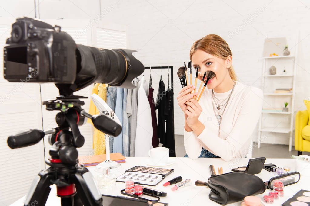 beauty blogger with decorative cosmetics holding cosmetic brushes in front of video camera