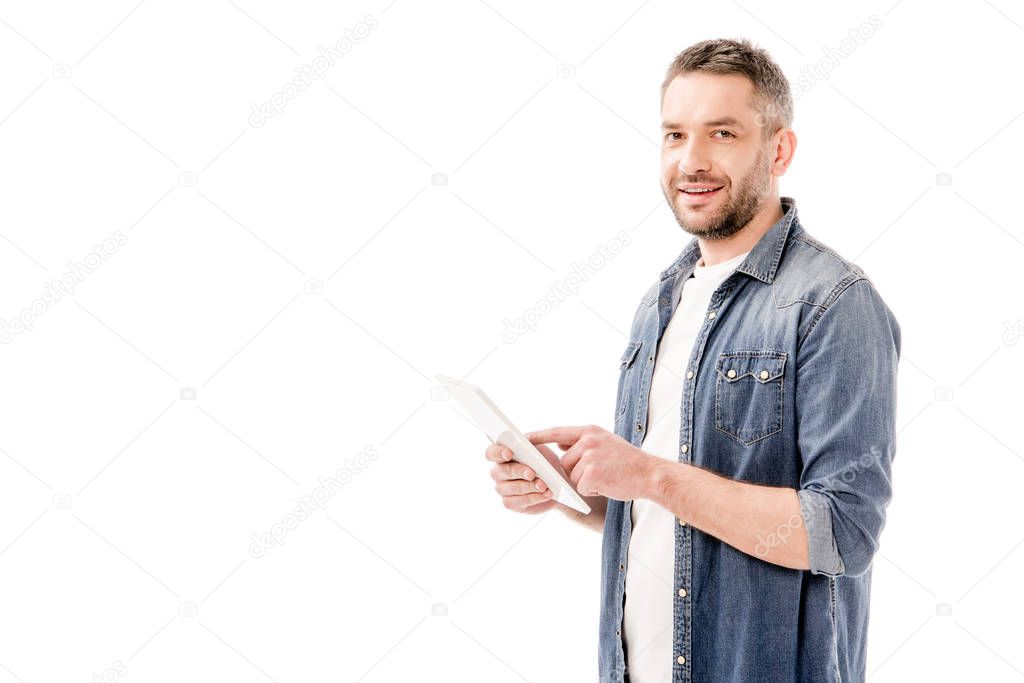 smiling bearded man in denim shirt using digital tablet and looking at camera isolated on white