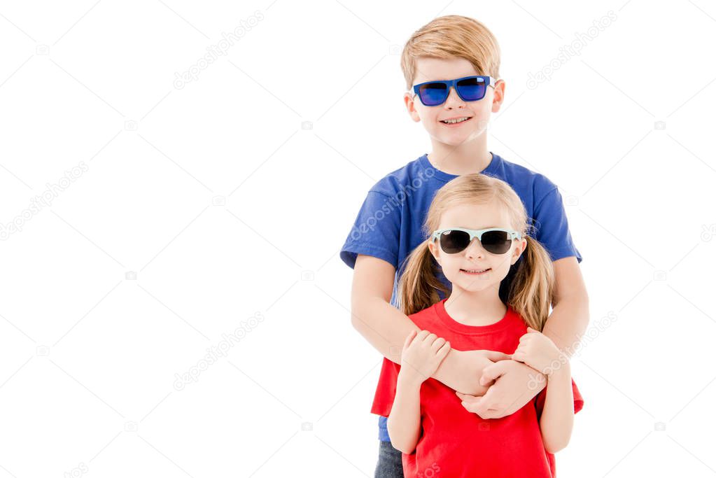 front view of sister and brother in sunglasses embracing isolated on white