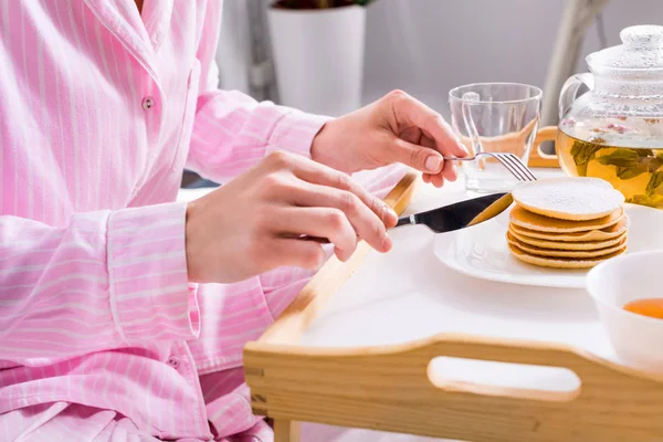 Partial view of woman in pajamas having pancakes for breakfast in bed at home — Stock Photo