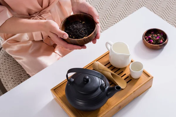 Tiro recortado de mujer sosteniendo tazón de madera con té negro en las manos en la mañana en casa - foto de stock