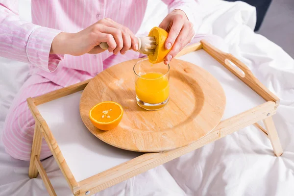 Visão parcial da mulher com pilão de madeira fazendo suco de laranja fresco na cama de manhã em casa — Fotografia de Stock