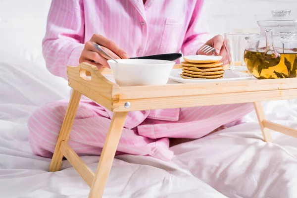 Vue partielle de la femme en pyjama ayant des crêpes pour le petit déjeuner au lit à la maison — Photo de stock