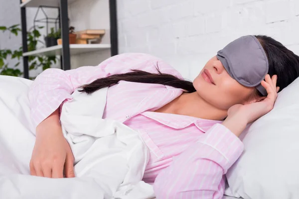 Retrato de mulher de pijama rosa e máscara de dormir dormindo na cama em casa — Fotografia de Stock