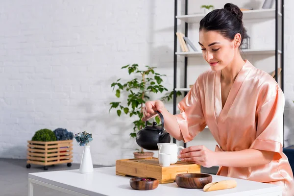 Attraktive Frau im Seidenbademantel, die Tee kocht, während sie morgens zu Hause Teezeremonie hat — Stockfoto