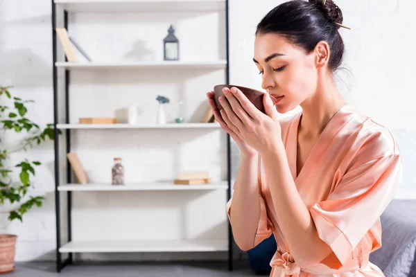 Woman in silk bathrobe with wooden bowl in hands having tea ceremony in morning at home — Stock Photo