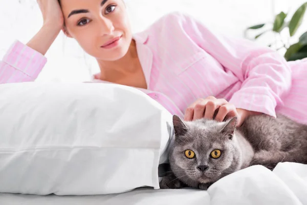 Portrait de femme séduisante en pyjama avec chat à poil court britannique reposant sur le lit à la maison — Photo de stock