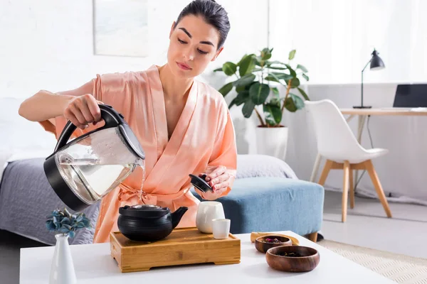 Mujer atractiva en albornoz de seda haciendo té durante la ceremonia del té en la mañana en casa - foto de stock