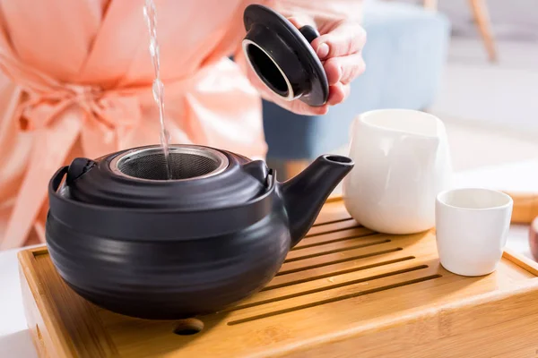 Tiro recortado de la mujer haciendo té mientras toma la ceremonia del té en la mañana en casa - foto de stock