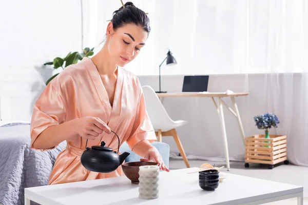 Mujer atractiva en albornoz de seda haciendo té durante la ceremonia del té en la mañana en casa - foto de stock