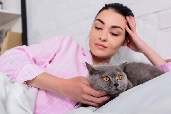 Retrato de mujer mirando britain shorthair gato mientras acostado en cama en casa - foto de stock