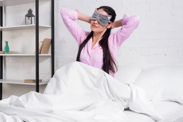 Portrait of woman in pink pajamas and sleeping mask stretching in bed in morning — Stock Photo