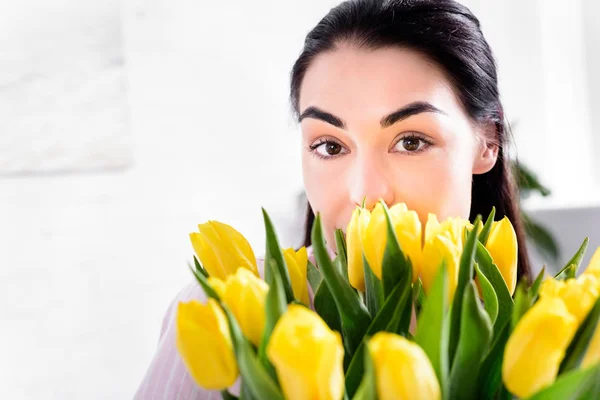 Vista parziale della donna con bouquet di tulipani gialli guardando la fotocamera a casa — Foto stock