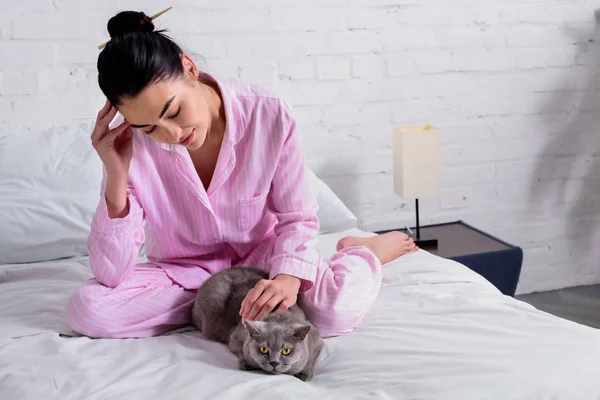 Жінка в піжамі з британським короткошерстим котом відпочиває на ліжку вдома — стокове фото