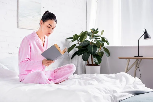 Woman in pajamas reading book on bed in morning at home — Stock Photo