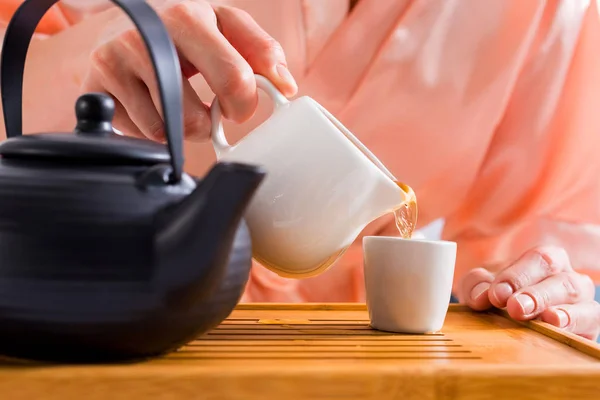 Visão parcial da mulher derramando chá na xícara ao ter cerimônia de chá em casa — Fotografia de Stock