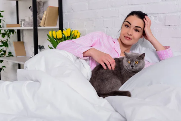 Portrait of woman with britain shorthair cat resting in bed at home — Stock Photo