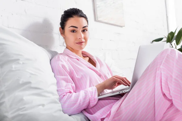 Vista laterale della donna in pigiama con computer portatile a letto a casa — Foto stock