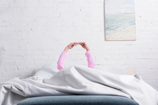 Partial view of woman in pajamas using smartphone while resting in bed at home — Stock Photo