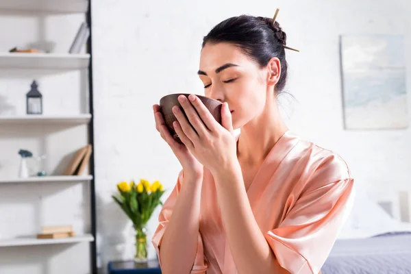 Donna in accappatoio di seta con ciotola di legno in mano con cerimonia del tè al mattino a casa — Foto stock