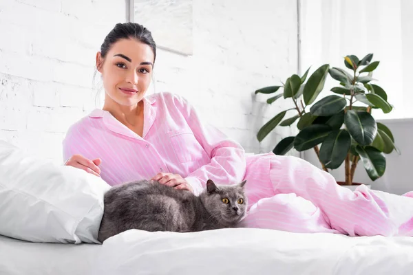 Mulher sorrindo com gato brecha britânico deitado na cama em casa — Fotografia de Stock