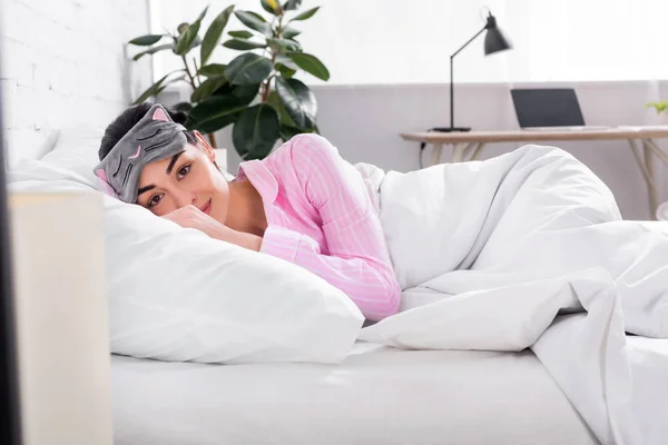 Ritratto di donna in pigiama rosa e maschera addormentata sdraiata a letto a casa — Foto stock