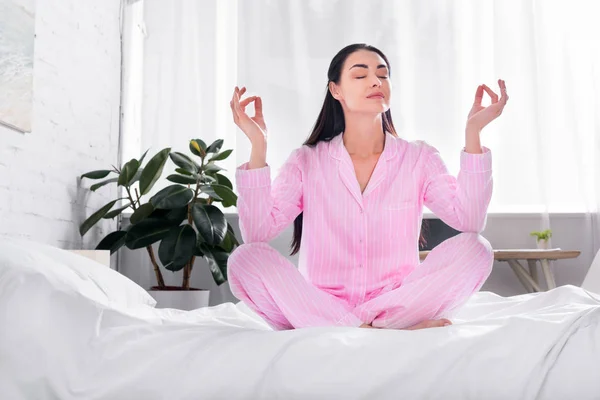 Woman in pink pajamas sitting in lotus pose on bed in morning at home — Stock Photo