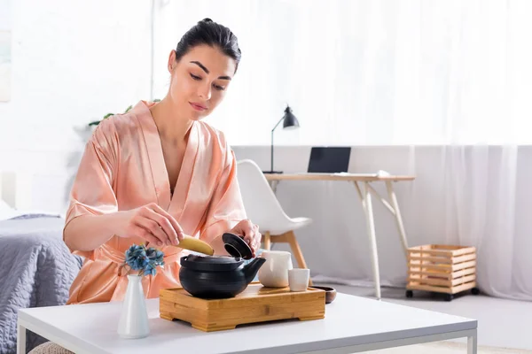 Mulher atraente em roupão de seda fazendo chá enquanto tendo cerimônia de chá de manhã em casa — Fotografia de Stock
