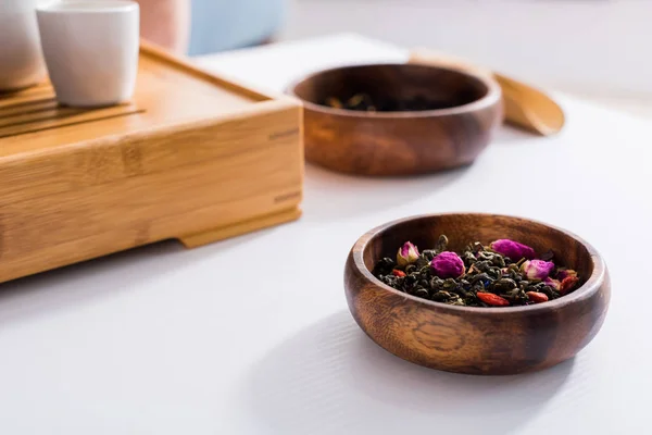 Vista de cerca de cubiertos de madera arreglados con té negro y flores para la ceremonia del té en la mesa blanca - foto de stock