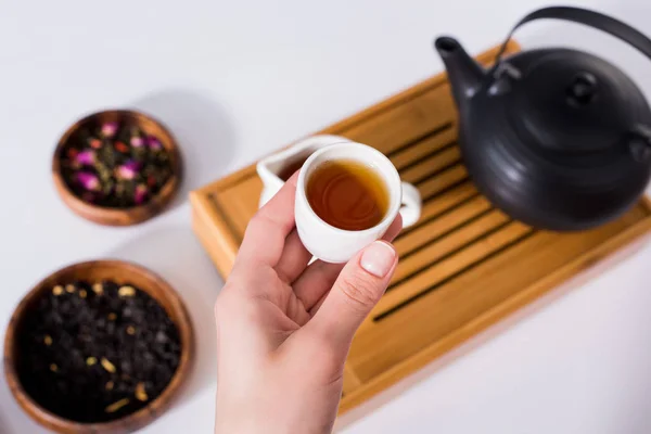 Plan recadré de la femme tenant une tasse de thé chaud tout en ayant cérémonie du thé à la maison — Photo de stock