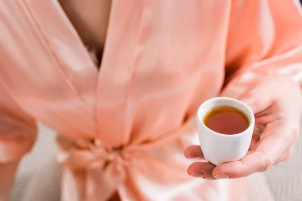 Обрізаний знімок жінки в шовковому халаті з чашкою гарячого чаю в руці — стокове фото