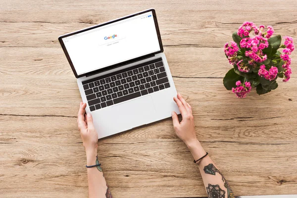 Vista parziale della donna da tavolo con computer portatile con logo google e pianta di kalanhoe in vaso da fiori — Foto stock